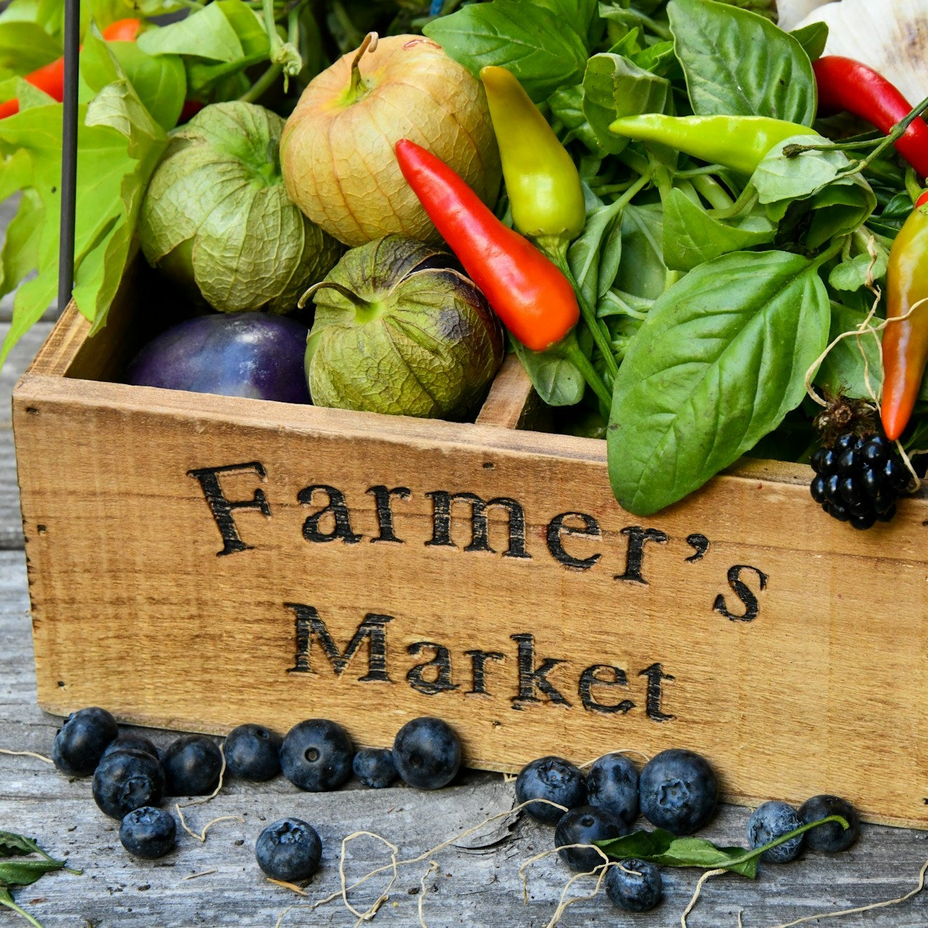 Wooden crate labeled 'Farmer's Market' filled with fresh produce on a wooden surface.